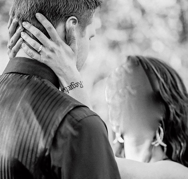Couple embracing, woman's hand shows tattoo fail, with fading black ink on wrist, adding a humorous element.