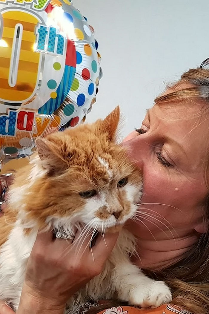 Woman holding and kissing an elderly cat with a colorful 30th birthday balloon in the background celebrating the cat's birthday. Woman holding and kissing an elderly cat with a colorful 30th birthday balloon in the background celebrating the cat's birthday.