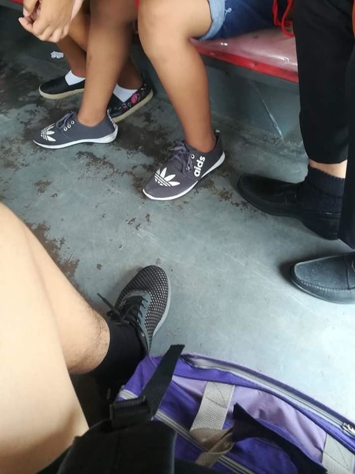 Unexpected clothing disaster with misspelled brand shoes on a bus floor, surrounded by passengers’ feet.
