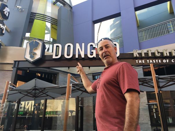 A dad humorously points at the "DONG" sign outside a restaurant, embodying classic funny dad antics.
