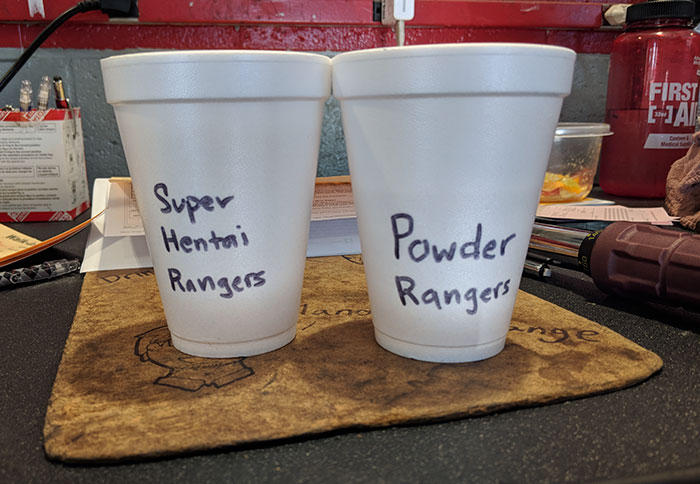 Two white cups on a desk labeled with stereotypical Asian and white coworker trolling humor.