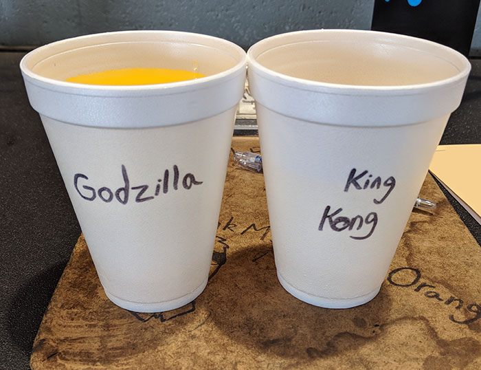 Two white cups labeled Godzilla and King Kong, showing coworkers hilariously trolling with Asian and white stereotypes.