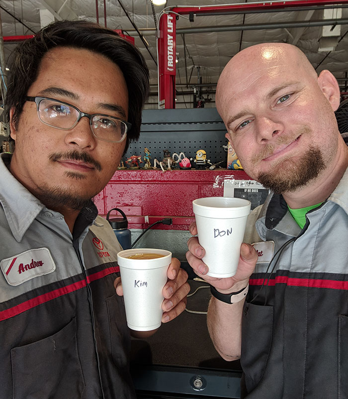 Two coworkers humorously troll each other using Asian and white stereotypes, holding coffee cups with swapped names.