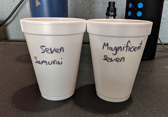 Two white foam cups on a desk labeled with Asian and white stereotypes as part of coworkers trolling each other.
