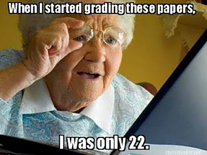 Elderly woman humorously grading papers, highlighting educator hardships with a laptop.