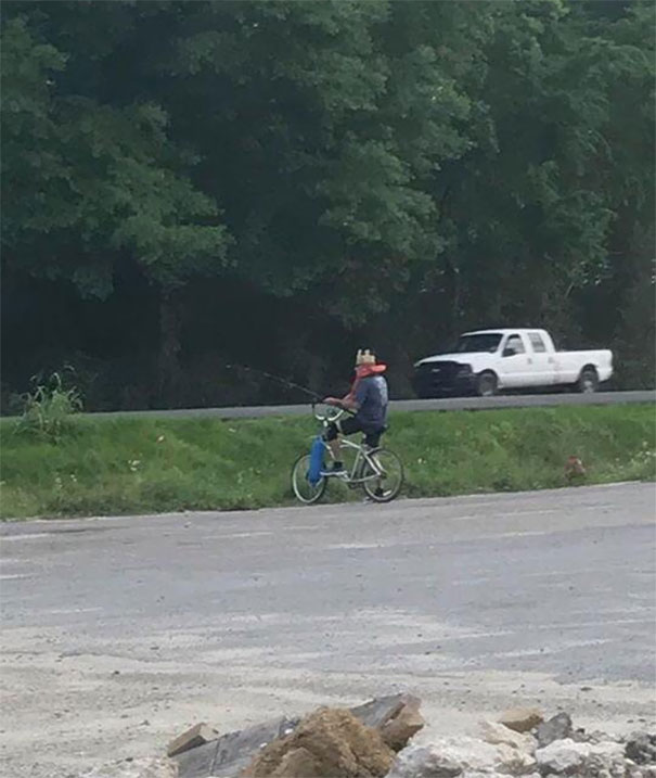 This Guy Is Fishing In A Empty Ditch On A Busy Highway Wearing A Life Jacket And Burger King Hat Sitting On A Bike That Has A Buoy Attached