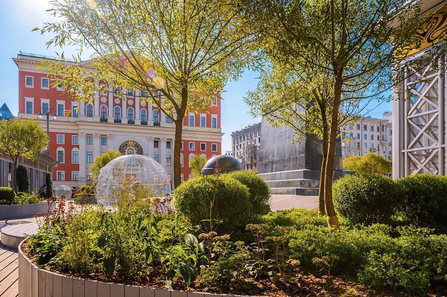 Sunny city park with blooming flowers and trees during the Flower Jam Festival in Moscow with historic buildings in background