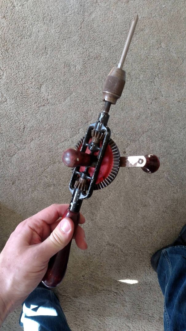 Funny dad holding an antique hand drill on a carpeted floor.