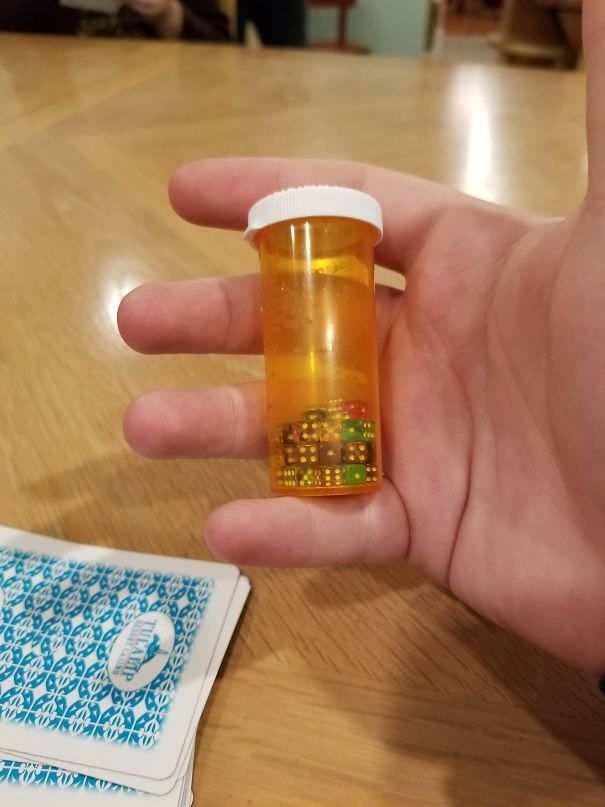 A dad holding a pill bottle filled with dice, next to a deck of playing cards, showcasing his humor in a playful setting.