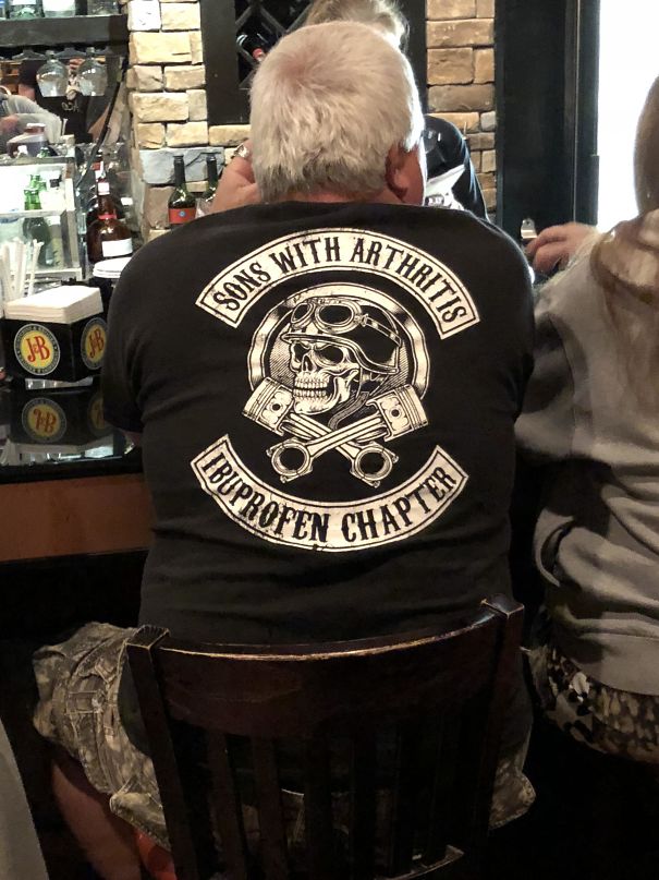 A man sitting at a bar, wearing a humorous "Sons with Arthritis, Ibuprofen Chapter" shirt.