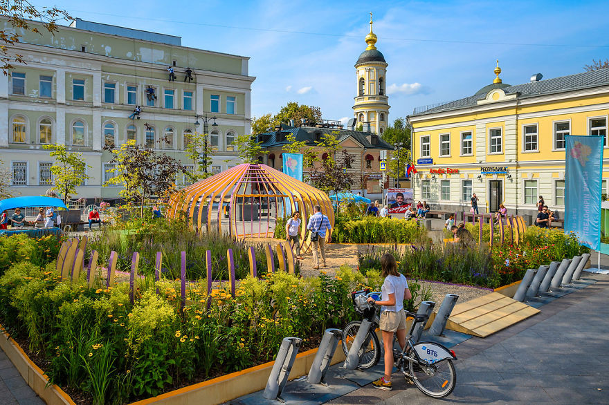 Flower Jam festival in Moscow featuring outdoor floral displays, visitors walking and a woman with a bicycle on a sunny day.