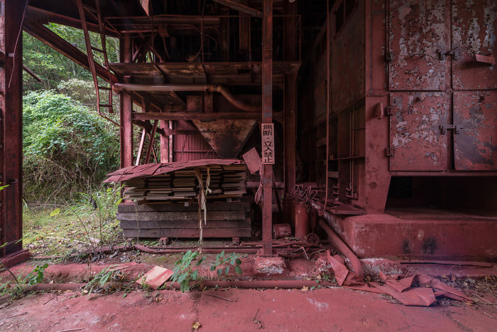 Abandoned industrial structure with rusted metal and overgrown vegetation in a remote location in Japan.