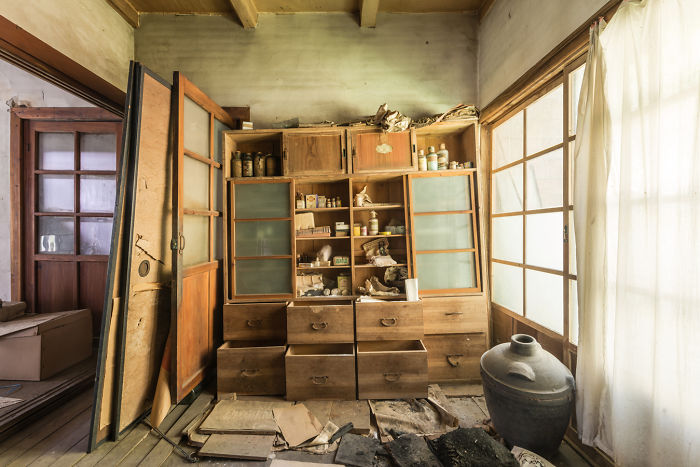 Abandoned place interior in Japan showing old wooden cabinets, broken drawers, scattered debris, and natural light through shoji screens.