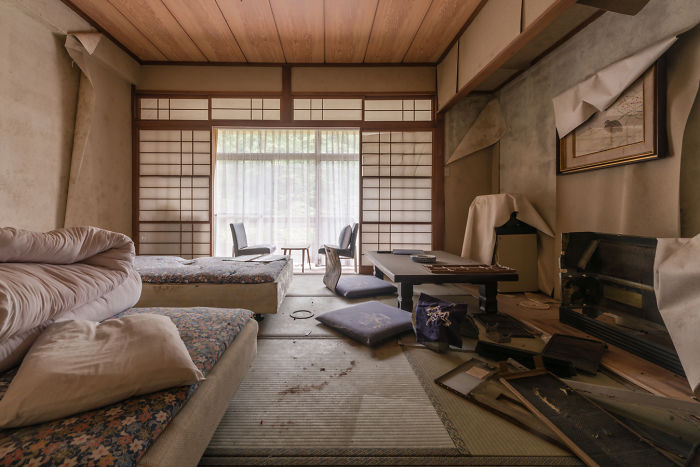 Abandoned places in Japan showing a neglected traditional room with tatami mats, scattered cushions, and old furniture.