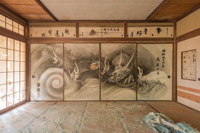 Abandoned traditional Japanese room with dragon mural on sliding doors and worn tatami mats inside a deserted building.