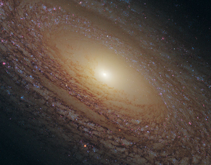 Spiral galaxy with glowing center and dusty arms, illustrating cosmic events related to Earth in the next trillion years.