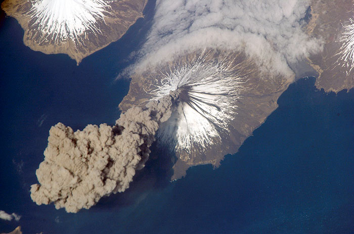 Volcanic eruption on Earth, showing ash plume and snow-capped mountain, highlighting future changes to Earth.