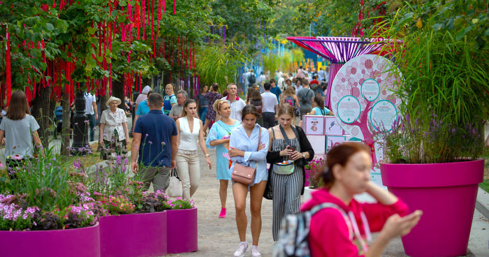 Crowd walking through colorful outdoor flower displays and installations at a vibrant flower jam festival in Moscow park.
