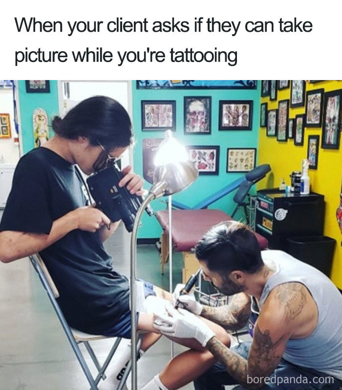 Tattoo artist working while a client amusingly records with a large camera, creating a humorous tattoo meme.
