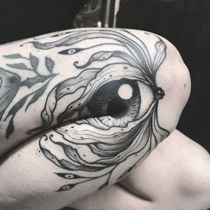 Genius tattoo forming an eye illusion on bent knee, revealing intricate details when extended. Genius tattoo forming an eye illusion on bent knee, revealing intricate details when extended.