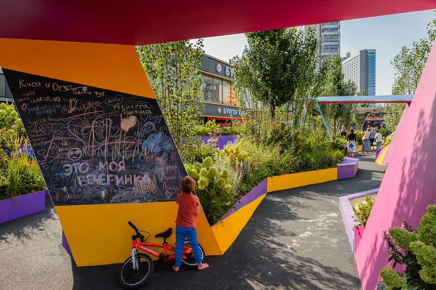Child writing on a colorful chalkboard surrounded by plants at the Flower Jam Festival in Moscow park area.