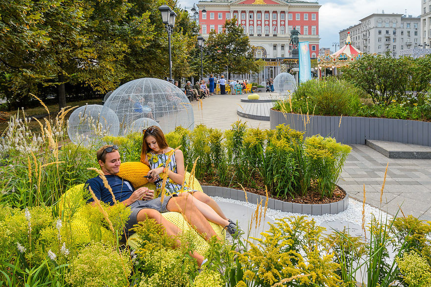 Couple relaxing among vibrant plants and flowers at Flower Jam Festival in a scenic Moscow park setting.
