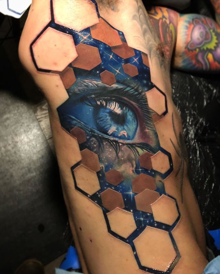 3D tattoo of a realistic blue eye and hexagonal pattern on skin, showcasing intricate artistry.