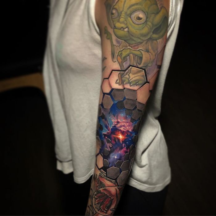 3D tattoo with hexagonal design and galaxy theme on forearm, featuring a small green creature.