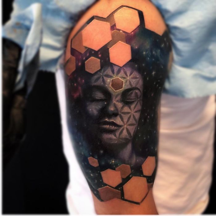 3D tattoo of a serene face with geometric patterns, showcasing intricate detail and depth on a person's upper arm.