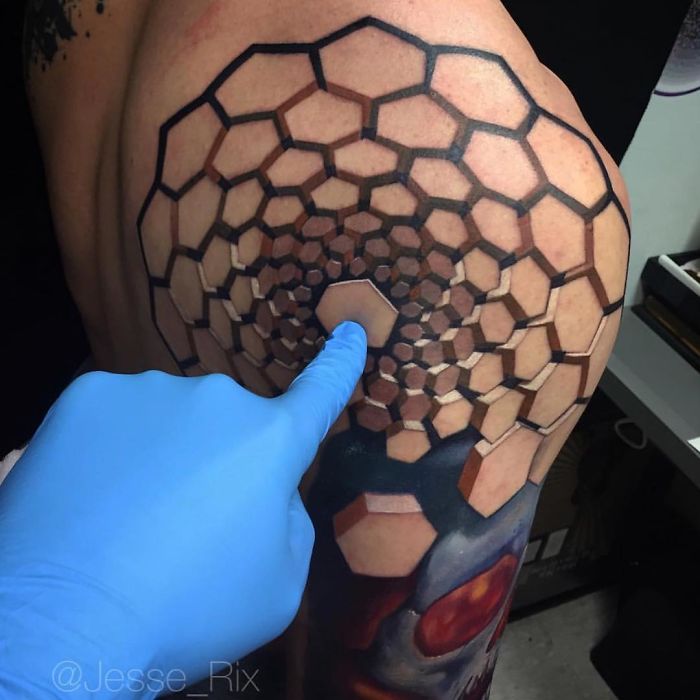 3D tattoo of hexagons creating an optical illusion, with a gloved hand touching it on a shoulder.