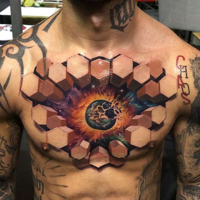 3D tattoo of a hexagonal pattern with an exploding Earth in the center, creating an optical illusion on a person's chest.