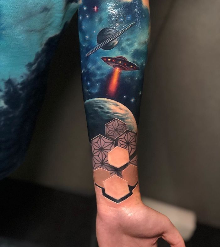 3D tattoo of space scene and geometric shapes on forearm.