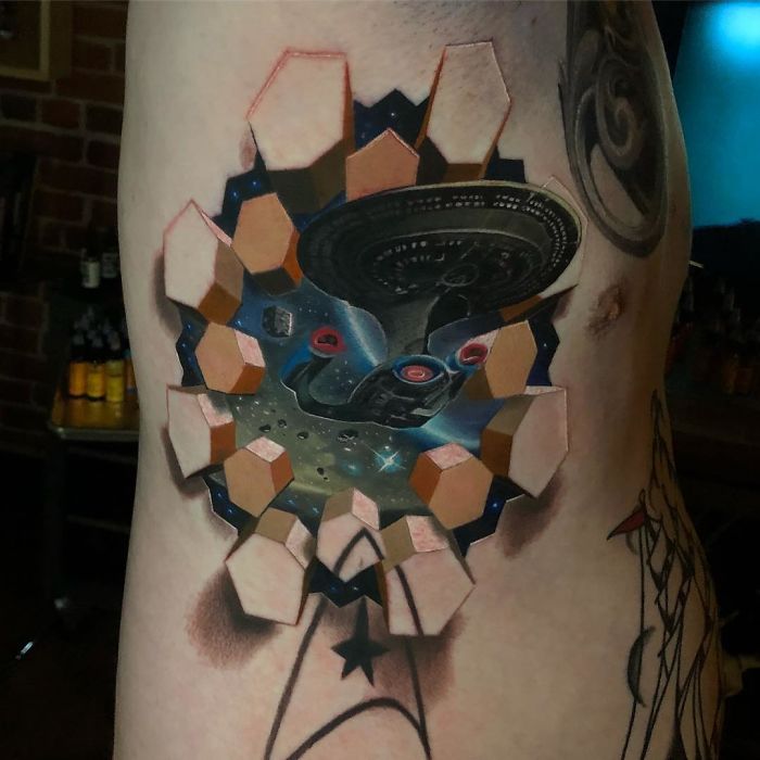 3D tattoo of spaceship emerging through a hexagonal portal on a person's side.