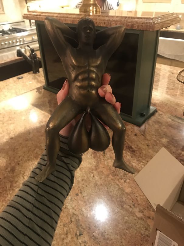 A person holding a humorous bronze sculpture in a kitchen.