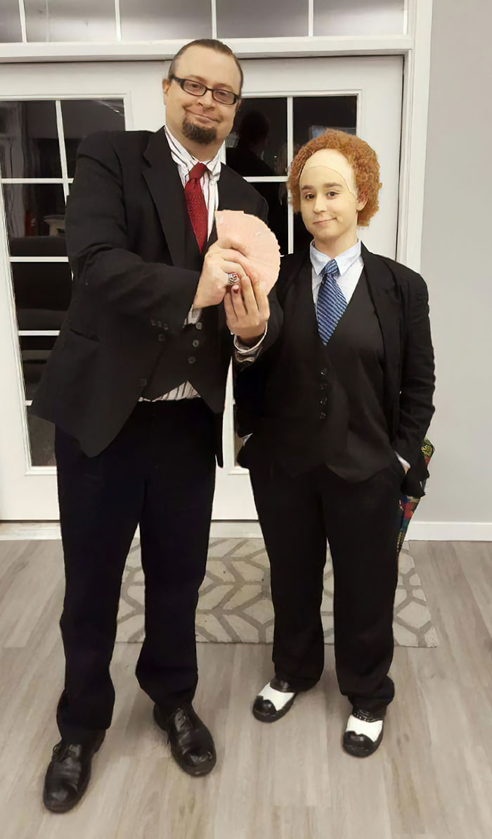 Couple dressed in matching costumes, holding a prop, celebrating Halloween.
