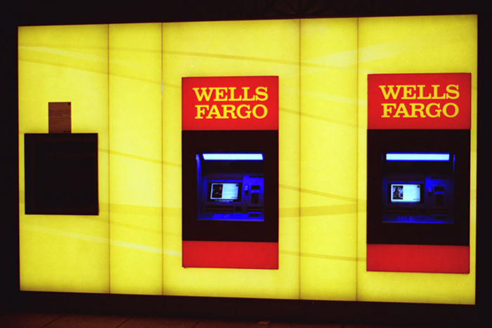 Two Wells Fargo ATMs built into a bright yellow wall, illuminated in a dark indoor setting with blue screen light.