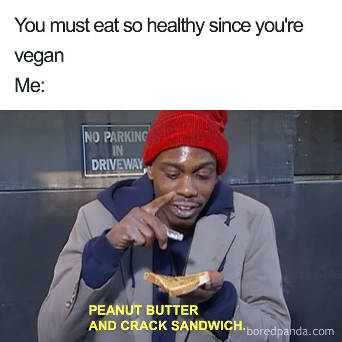 Man in a red beanie humorously mimics a vegan meme with a peanut butter sandwich in hand.