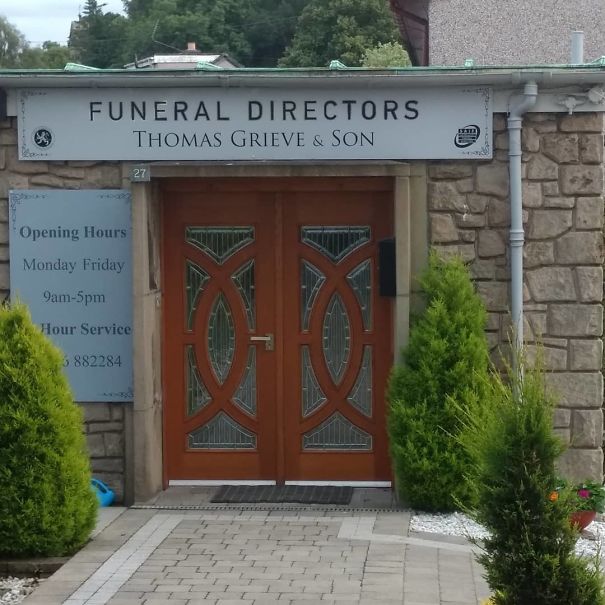 "Entrance of a funeral directors' office, showing distinct wooden doors and an ironic business name above."