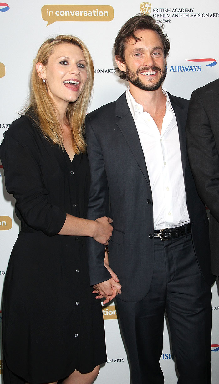 Two celebrities smiling and holding hands at an event, representing celebrities who fell in love while acting together.