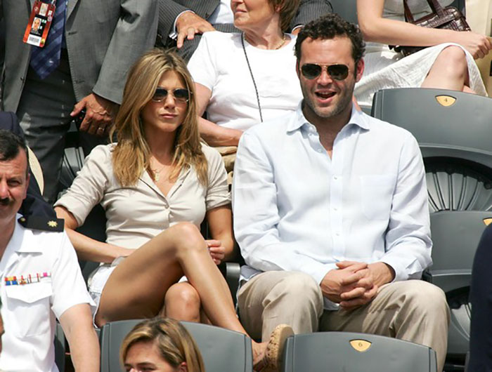 Two celebrities wearing sunglasses sitting together in a crowd, highlighting celebrities who fell in love while acting together.