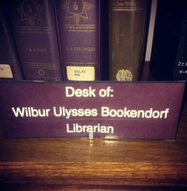 Librarian's desk sign humorously named Wilbur Ulysses Bookendorf in a library setting.