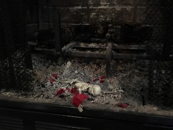 "Elf On The Shelf idea with elf clothes and a small skeleton placed in fireplace ashes, humorously suggesting the elf met an unfortunate fate."