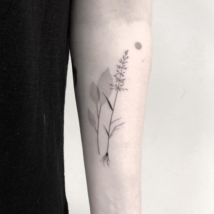 Minimalist botanical tattoo on forearm, featuring delicate leaves and stems in black ink.