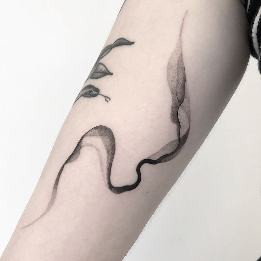 Minimalist tattoo featuring botanical illustration with abstract lines on forearm.