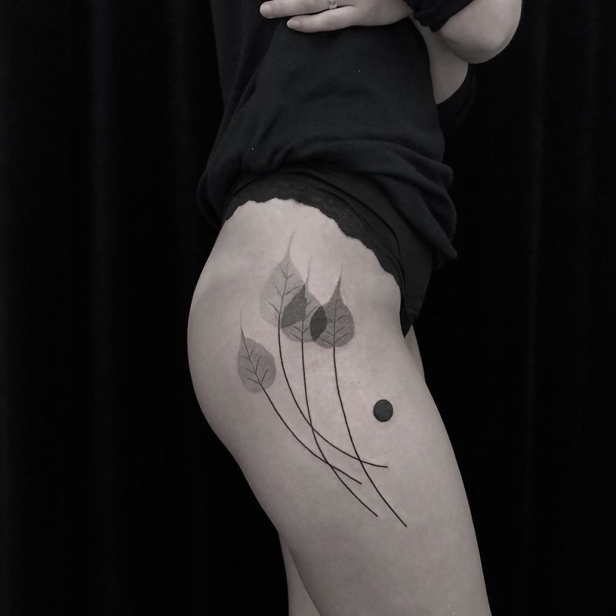 Minimalist botanical tattoo on thigh with delicate leaf designs and artistic linework.