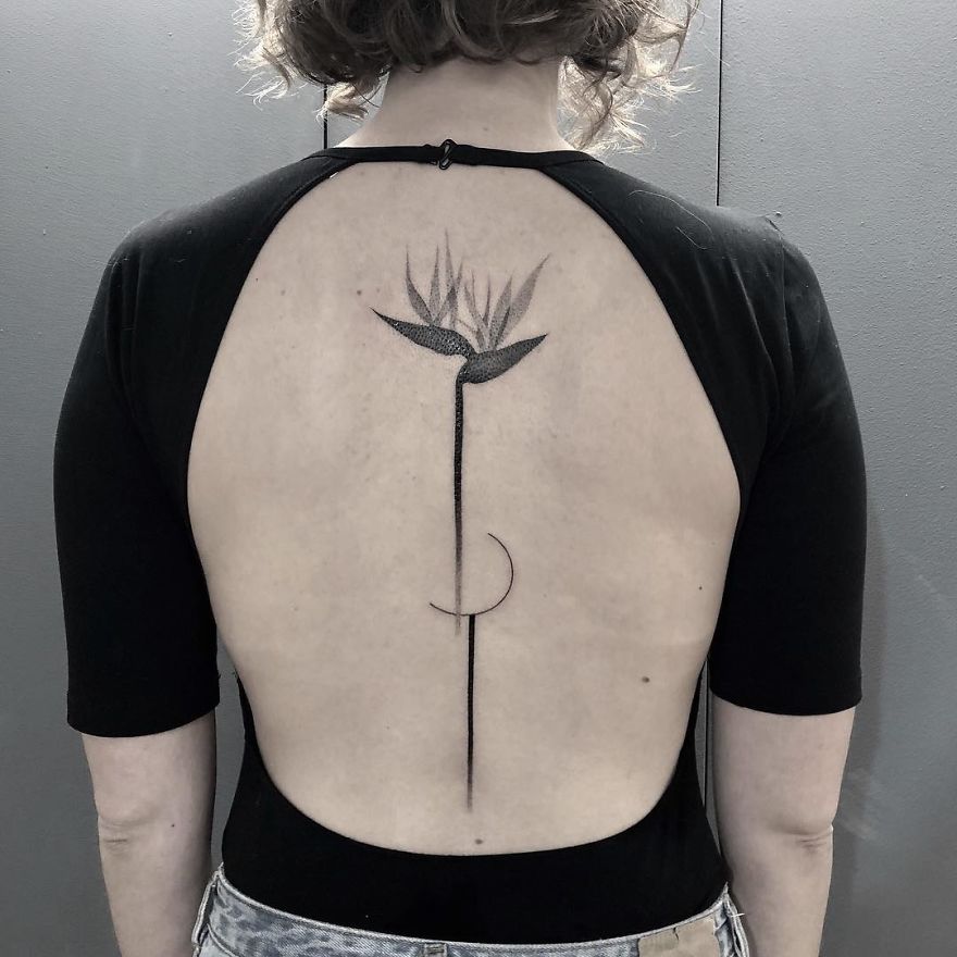 Minimalist botanical tattoo on back, featuring a stylized flower and crescent design.