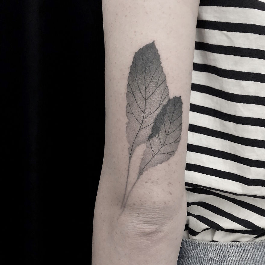 Minimalist tattoo of botanical leaves on an arm, placed against a striped shirt.
