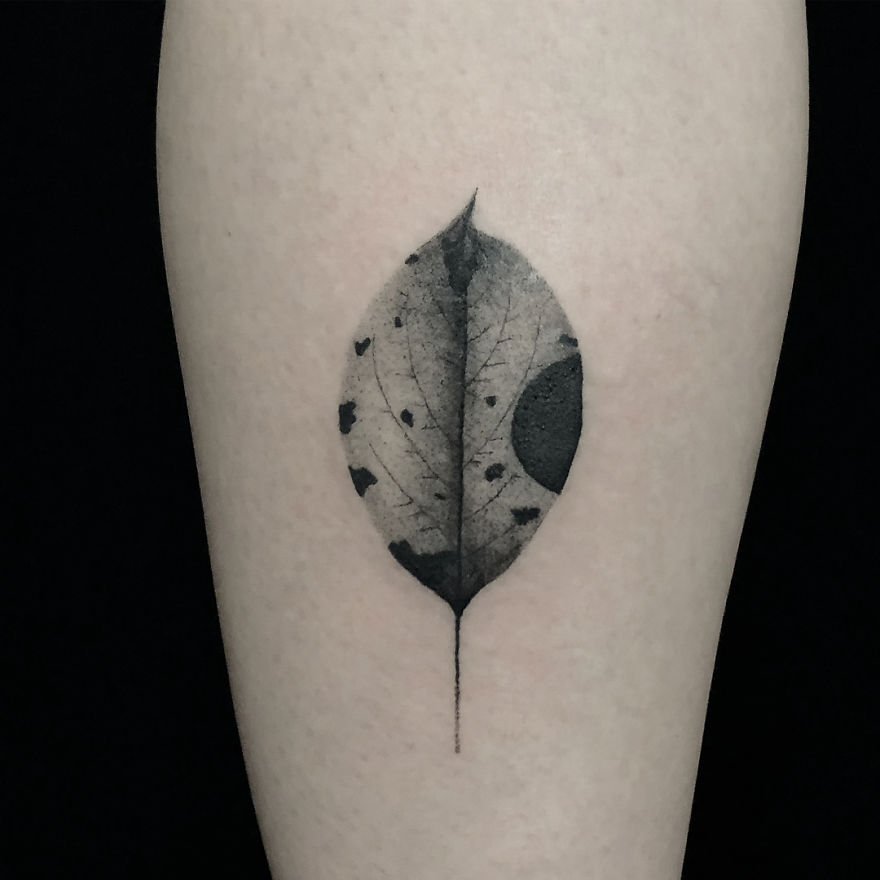 Minimalist botanical tattoo of a leaf with dark accents on skin.