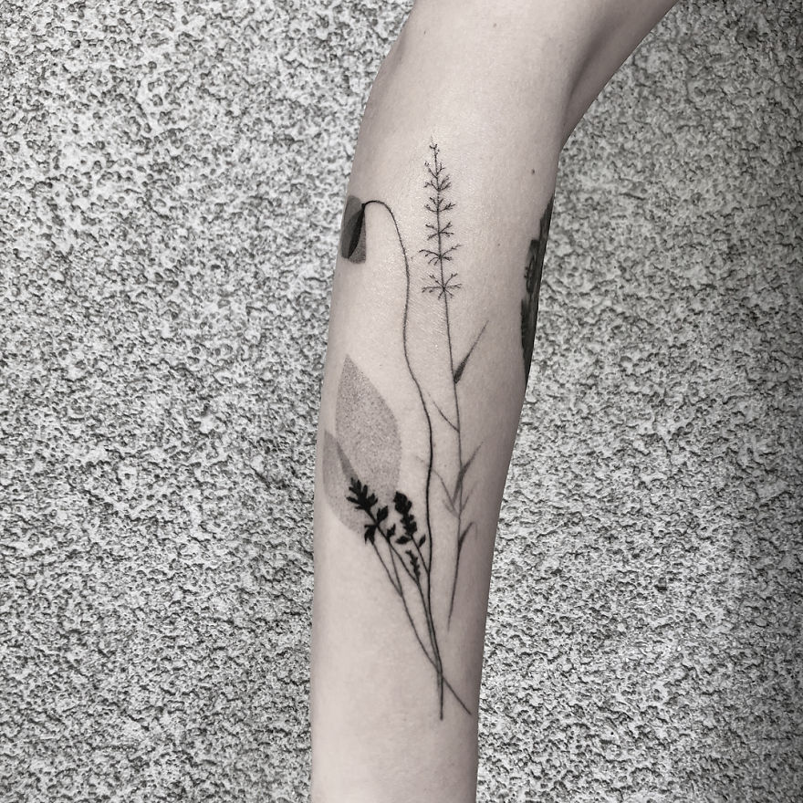 Minimalist botanical tattoo design on a forearm, featuring delicate plant illustrations.