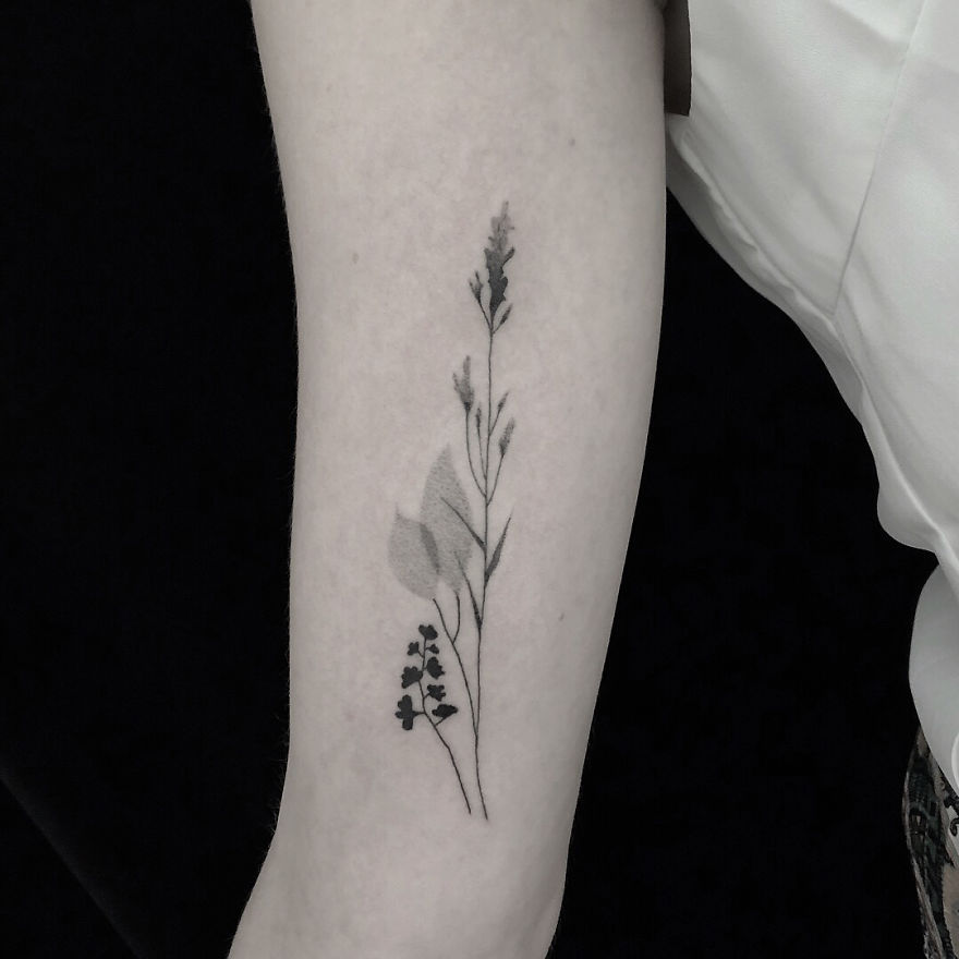 Minimalism and botanical tattoo design on a person's forearm, featuring delicate plant motifs.